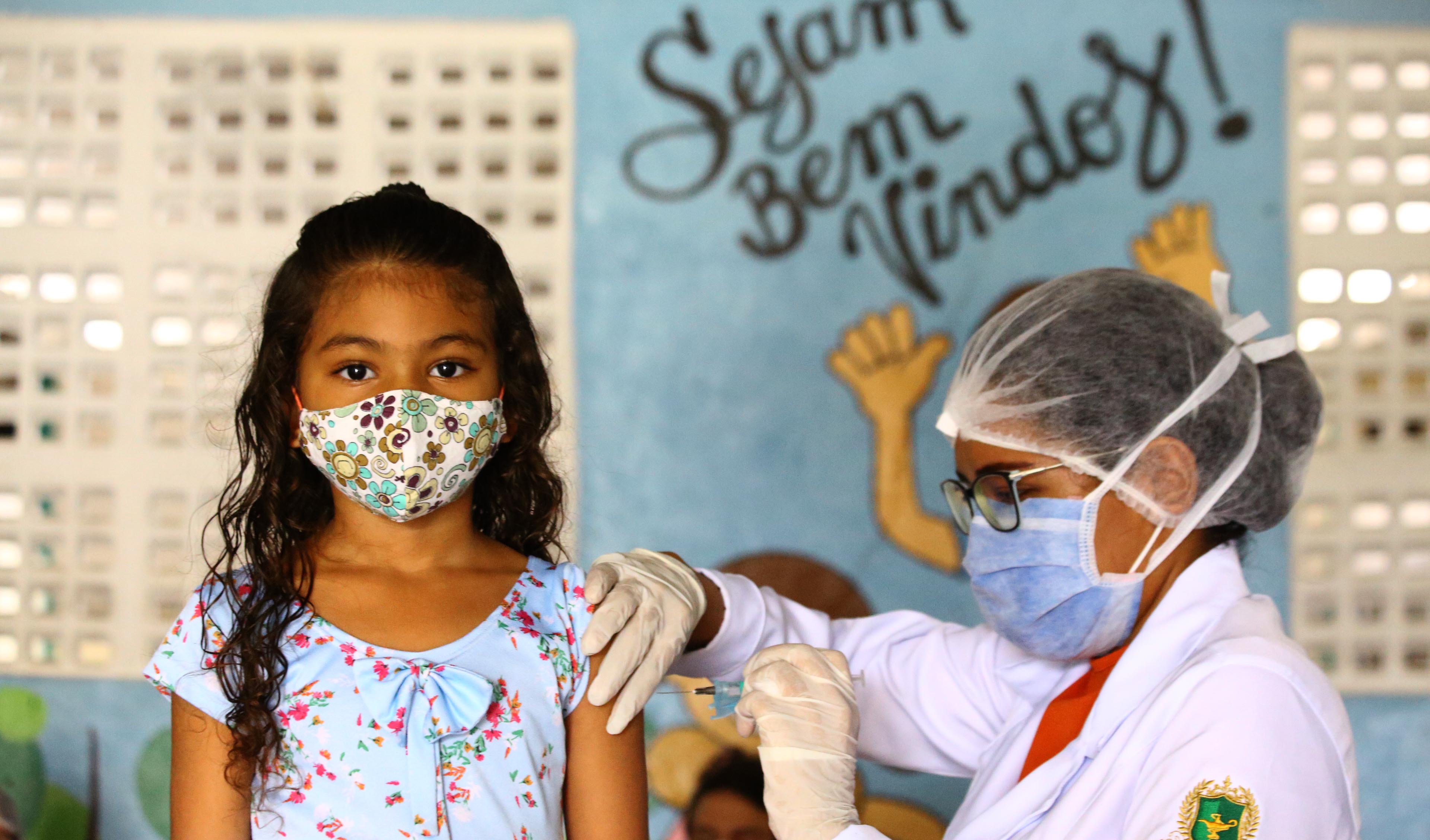 uma enfermeira vacina uma menina. Ambas usam máscara